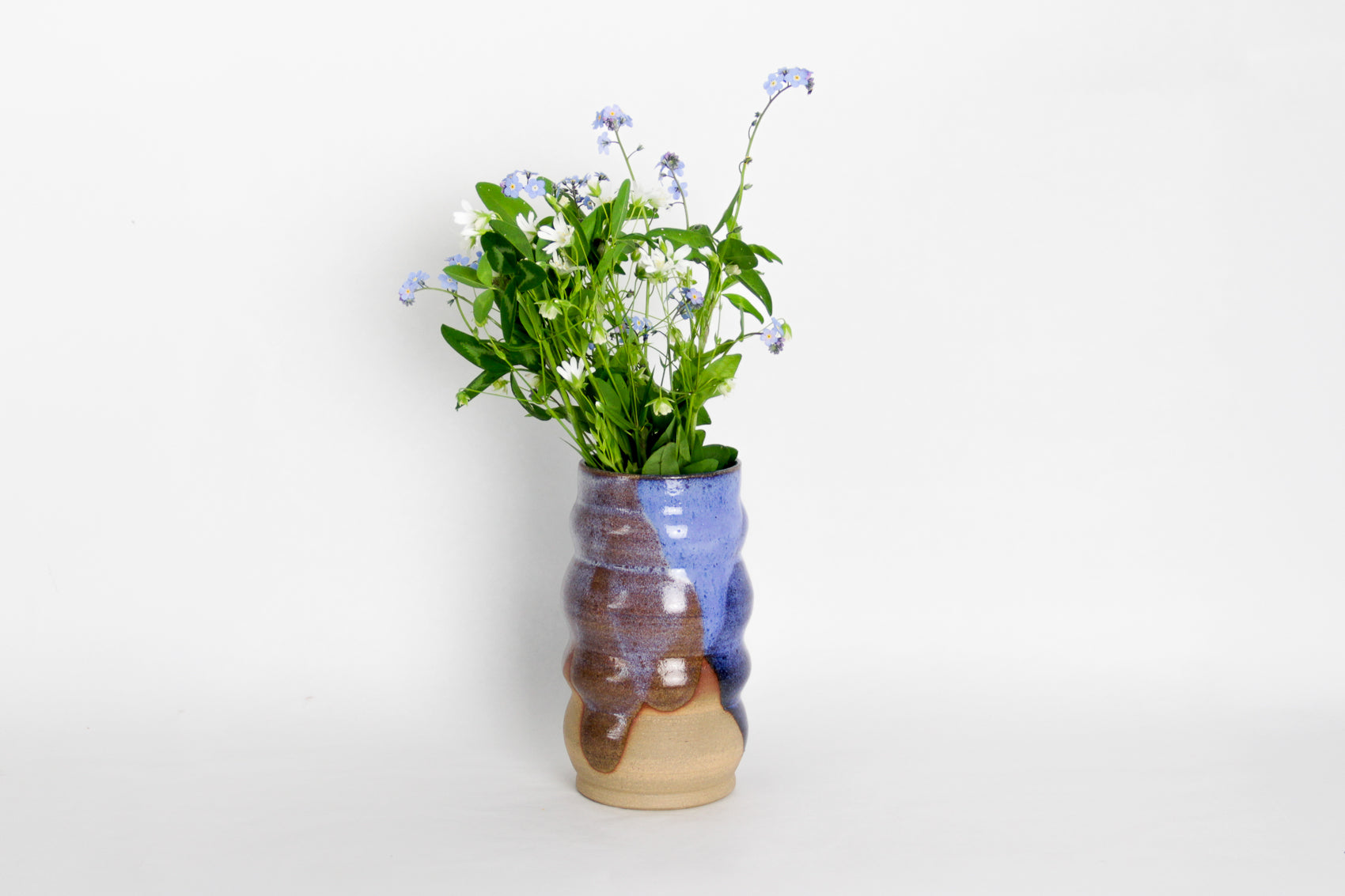 Image d'un vase avec un bouquet de fleur. Le vase en céramique est bicolore. Sa forme est irrégulière et moderne.